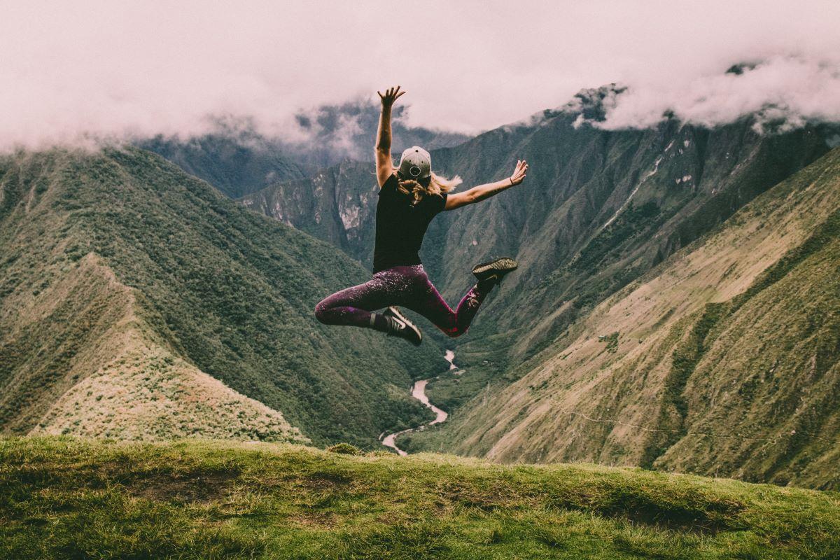 Excited individual leaping amid stunning mountain vista overlooking a river, inspired by hot sauce adventure